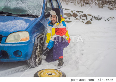Winter accident on the road. A man changes a wheel during a snowfall. Winter problems 61823626