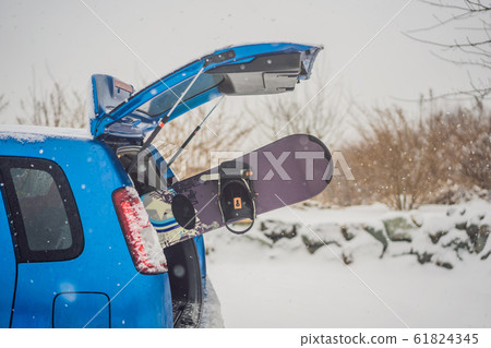 The snowboard does not fit into the car. A snowboarder is trying to stick a snowboard into a car 61824345