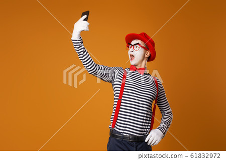 Young mime in white gloves and red hat takes selfie on orange background Young mime in white gloves and red hat takes selfie on orange background 61832972