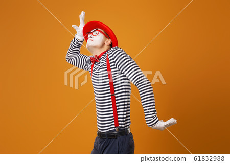 Mime male in red hat and in vest pointing on orange background 61832988