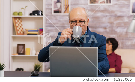 Old man enjoying a cup of coffee while working on laptop Old man enjoying a cup of coffee while working on laptop 61833069