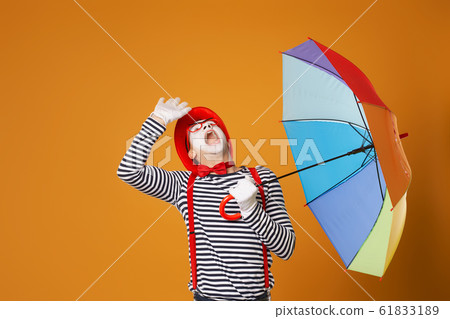 Mime man looking up with multi-colored umbrella isolated on empty orange background in studio Mime man looking up with multi-colored umbrella isolated on empty orange background in studio 61833189
