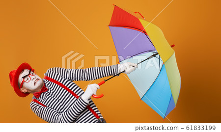 Mime with multi-colored umbrella during wind isolated on empty orange background 61833199