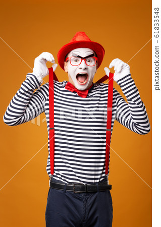 Happy mime looking at camera in vest and red hat Isolated on orange background 61833548