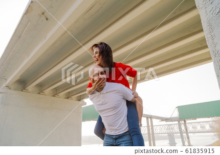Happy girl on the back of a man at the bridge Happy girl on the back of a man at the bridge 61835915