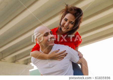 Happy girl on the back of a man at the bridge Happy girl on the back of a man at the bridge 61835936