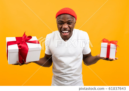 funny african man with a smile in a white t-shirt holds two boxes a gift with a red ribbon for 61837643