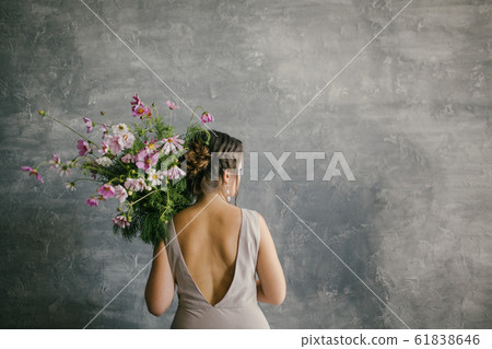 A young Beautiful Girl in a Pink Dress Holding a Delicate Bouquet of Flowers on a Gray Background 61838646