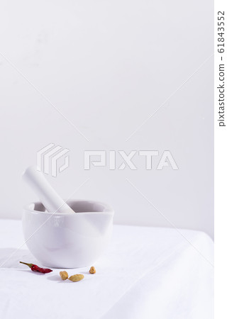 White porcelain mortar and pestle with chili peppers and cardamom isolated on textile table, copy space 61843552
