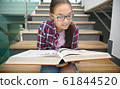 Girl is reading book while sitting on stairs 61844520