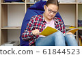 Girl is reading book while sitting in room 61844523