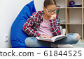 Girl is reading book while sitting in room 61844525