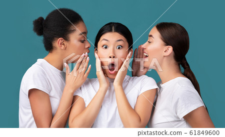 Three Girlfriends Sharing Secrets Standing On Turquoise Background In Studio Three Girlfriends Sharing Secrets Standing On Turquoise Background In Studio 61849600