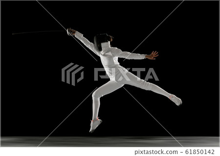 Teen girl in fencing costume with sword in hand isolated on black background 61850142