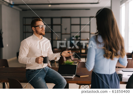 Young businessman holds cup of coffee and communicates with his colleague 61850400