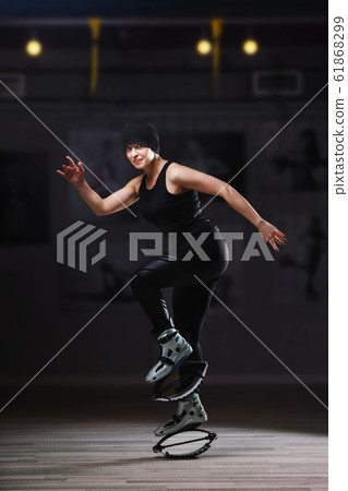 Smiling woman in a black sportswear jumping in a kangoo jumps shoes 61868299