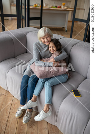 Grandmother and granddaughter sitting hugging on a sofa. Grandmother and granddaughter sitting hugging on a sofa. 61868360