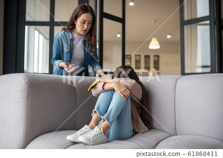 Crying daughter hiding her face and mom standing next to her. Crying daughter hiding her face and mom standing next to her. 61868411