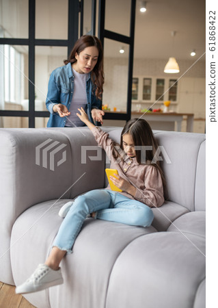 Naughty daughter with smartphone in her hand sitting on couch. Naughty daughter with smartphone in her hand sitting on couch. 61868422