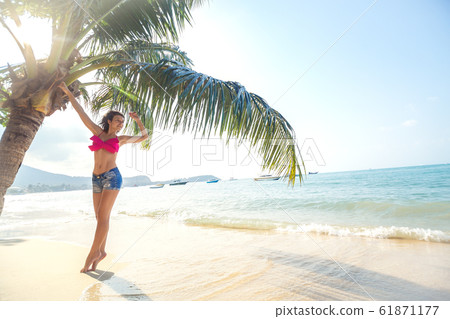 Sexy slim girl near a palm tree on the shore of a Sexy slim girl near a palm tree on the shore of a 61871177