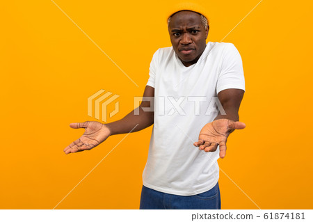 charismatic african man in a white t-shirt with a layout outraged in surprise on a yellow studio 61874181