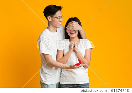 Asian guy covering girl eyes, making proposal with beautiful ring 61874748