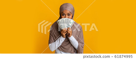 Happy Black Muslim Woman In Headscarf Covering Face With Dollar Cash Happy Black Muslim Woman In Headscarf Covering Face With Dollar Cash 61874995