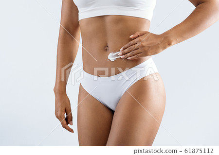 Afro woman applying cream on her well fit belly Afro woman applying cream on her well fit belly 61875112