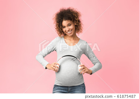 Pregnancy therapy. Afro woman holding headphones on her belly Pregnancy therapy. Afro woman holding headphones on her belly 61875487