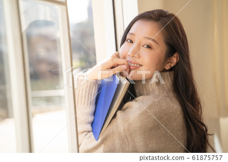 Beautiful young woman reading while sunbathing by the window Beautiful young woman reading while sunbathing by the window 61875757