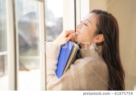 Beautiful young woman reading while sunbathing by the window Beautiful young woman reading while sunbathing by the window 61875759