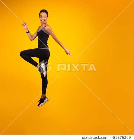 African American Lady Jumping Over Yellow Studio Background 61876209