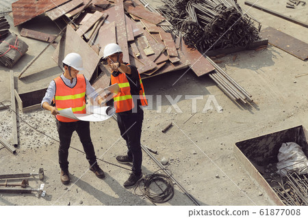 Two engineers work on the construction site. They Two engineers work on the construction site. They 61877008