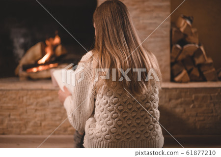 Pretty girl in sweater sitting by the fireplace Pretty girl in sweater sitting by the fireplace 61877210