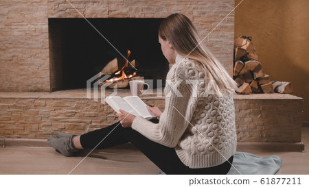 Beautiful woman sitting by the fireplace in sweater Beautiful woman sitting by the fireplace in sweater 61877211