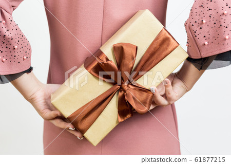 Girl holds a gift behind her back. Girl holds a gift behind her back. 61877215