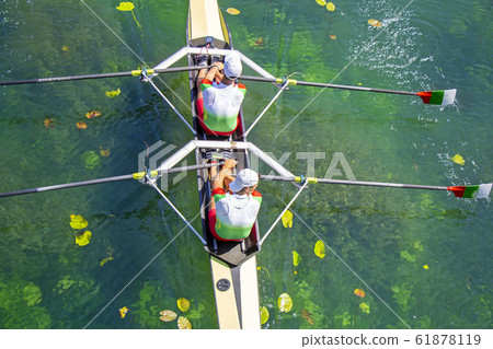 Two young athletes rowing team on green lake Two young athletes rowing team on green lake 61878119