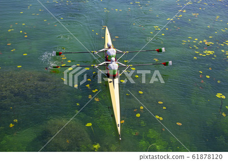 Two young athletes rowing team on green lake Two young athletes rowing team on green lake 61878120