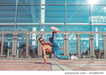 Male break-dancer, muscular torso, dancer, young guy, summer city, dancing street dances, modern youth style. Fashion and fitness sport motivation. Free space for copy text. Background glass doors. Male break-dancer, muscular torso, dancer, young guy, summer city, dancing street dances, modern youth style. Fashion and fitness sport motivation. Free space for copy text. Background glass doors. 61880344