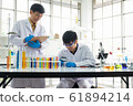 Science, Chemistry, Technology, Biology and Laboratory concept - Asian Senior scientist taking notes while Asian junior scientist looks into something on a petri dish. 61894214