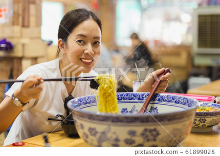 Happy smiling woman eating big bowl of noodle soup in Chinese restaurant. 61899028