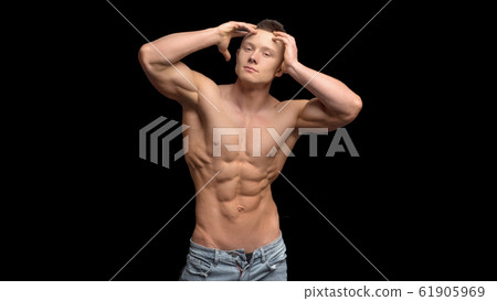 Shirtless, fitness shaped muscular men with perfect sporty body only in jeans with arms raised to a head posing at black background 61905969