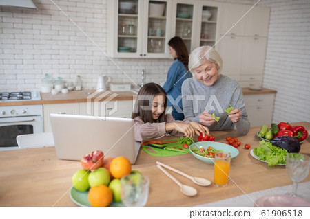 Grandmother and granddaughter cooking fresh vegetable salad. Grandmother and granddaughter cooking fresh vegetable salad. 61906518