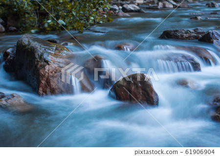 Clear river running fast, hitting rocks. 61906904