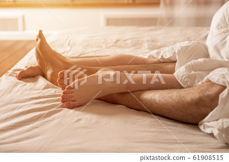 Men's and women's legs stick out from under the blanket. Men's and women's legs stick out from under the blanket. 61908515