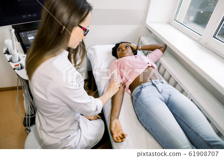Ultrasound, physiotherapy, rehabilitation concept. Young woman doctor physiotherapist sonographer examining the elbow with an ultrasound scan of her African female patient Ultrasound, physiotherapy, rehabilitation concept. Young woman doctor physiotherapist sonographer examining the elbow with an ultrasound scan of her African female patient 61908707