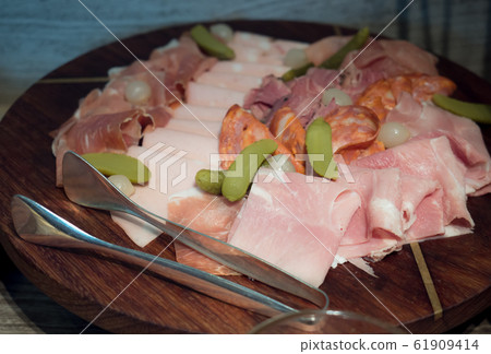 Assortment of tasty and delicious Italian antipasto charcuterie delicatessen. Parma ham, Chorizo, Salami with pickles on wooden plate. Assortment of tasty and delicious Italian antipasto charcuterie delicatessen. Parma ham, Chorizo, Salami with pickles on wooden plate. 61909414