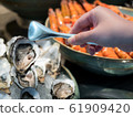Hand of Asian woman pick a tasty fresh shucked oyster on ice with tongs. 61909420