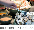 Hand of Asian woman pick a tasty fresh shucked oyster on ice with tongs. 61909422