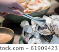 Hand of Asian woman pick a tasty fresh shucked oyster on ice with tongs. 61909423